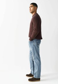 Bordo adīts džemperis, gaiši zili džinsi un brūni zamša apavi. Džemperim ir ribotas piedurknes; džinsiem ir aizmugurējās kabatas ar šuvēm.