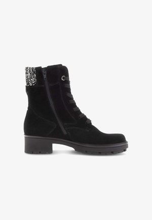 Bottine en suede noir avec une semelle en caoutchouc, à lacets sur le devant et fermeture éclair sur le côté. Elle présente un accent en tissu texturé noir et blanc au niveau du col.