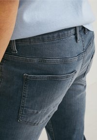 Mörkblå jeans med en texturerad denimtyg, femfickorsdesign, med en synlig bakficka och kontrasterande sömdetaljer.