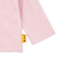 Maglione a maglia rosa chiaro con maniche lunghe, orlo a zig zag e un'etichetta gialla con logo di un orso. La morbidezza è evidente nel tessuto.