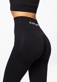 Black high-waisted leggings made from stretchy fabric, featuring textured panels and a gathered detail at the rear with "carpathe" logo on the waistband.