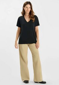 Zwart T-shirt met V-hals en korte mouwen, gecombineerd met lichtbeige broek met wijde pijpen. Gladde textuur, casual pasvorm en zonder opvallende patronen.