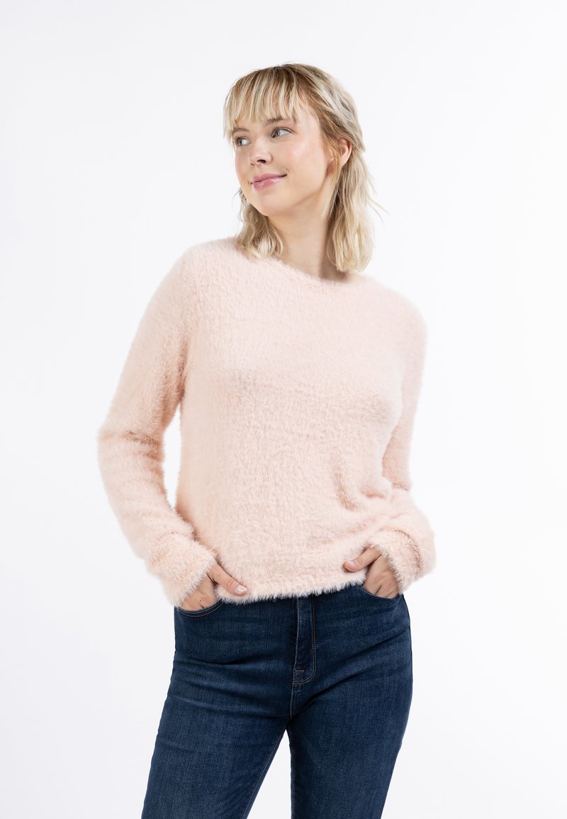 Helles rosa, flauschiges Sweatshirt mit langen Ärmeln, runder Ausschnitt und gerippten Manschetten. Kombiniert mit dunkelblauen Jeans aus Denim. Weiche Textur.
