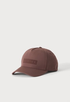 Brun Oakley baseballkasket med buet skygge og syet logo-mærke foran, vist mod en ensfarvet lys baggrund.