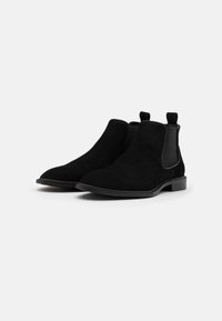 Bottines Chelsea en daim noir avec panneaux latéraux élastiques, semelles plates en caoutchouc et détails de boucle. Caractéristiques d'une texture lisse et d'une forme de pointe.