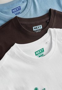 Kolme sinistä, ruskeaa ja valkoista taiteltua pyöreäkauluspaitaa, joissa kussakin on koko medium ja merkintä "NEXT Relaxed Fit".
