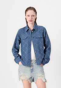 Jeansjakke med quiltet diamantmønster, to brystlommer, sølvknap-lukninger, og matchende slitte denimshorts med dekorasjoner.