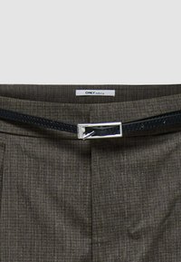 Pantaloni a quadri marroni con una cintura in pelle scura e fibbia in argento. Il tessuto ha una sottile texture e dettagli di vestibilità sartoriale.