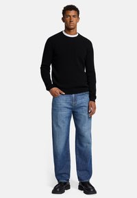 Maglione nero a coste con scollatura a girocollo, abbinato a jeans a gamba dritta blu chiaro e scarpe nere con lacci. Design e texture semplici.
