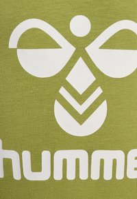 Grön textil med en stor vit logotyp som har tre former: två böjda vingar, en diamant och ett cirkulärt element, mot en ribbad struktur.