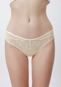 Culotte en dentelle pour femmes en beige clair avec motif floral, présentant une taille élastique douce et une finition délicate. Détails en mesh transparent visibles.