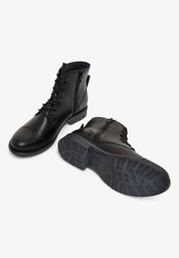 Bottines en cuir noir avec un bout rond, lacet à l'avant, fermeture éclair sur le côté, semelle en caoutchouc texturée et finition lisse.