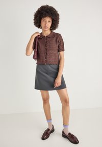 Καφέ υφασμένη κοντομάνικη κάρντιγαν με γιακά, συνδυασμένη με γκρι φούστα Α γραμμής, μπλε κάλτσες με μοτίβο και σκούρες λοφέρ.