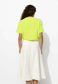 Haut à manches courtes jaune néon associé à une jupe midi blanche. La jupe a une texture lisse et une couture visible au centre.