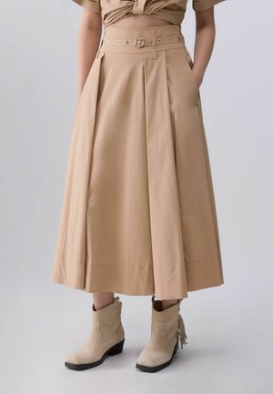 Beige midi-nederdel med plisseringer og bælte, båret med lysebrune ankelstøvler med lave hæle og kvastdetalje.