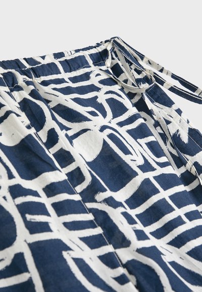 Granatowa tkanina z abstrakcyjnym białym geometrycznym wzorem, wyposażona w elastyczną talię i przymocowany wąski pasek z tkaniny.