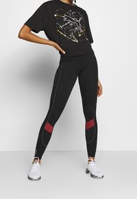 Černé tričko s barevným nástřikem a logem Puma; doplněné černými legínami s červenými akcenty a kontrastním prošitím.