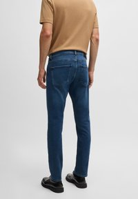 Dark blue denim jeans with a straight leg cut, five pockets, and a classic design. Worn with a beige textured short-sleeve shirt.