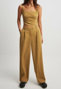 Musztardowa crop top z kwadratowym dekoltem i cienkimi ramiączkami, w połączeniu z szerokimi spodniami z przodowymi zaszewkami i kieszeniami bocznymi.