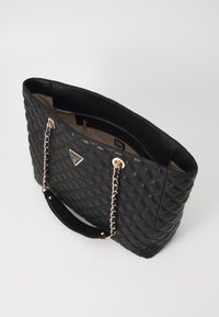 Bolsa tote negra acolchada con un asa acentuada con cadena, herrajes dorados, forro interior suave y un detalle de logo distintivo en la parte frontal.