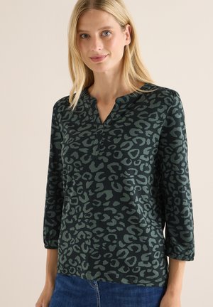 Haut à manches longues de couleur vert foncé avec un motif léopard, doté d'un col à renfoncement et d'un tissu texturé. Associé à un jean bleu.