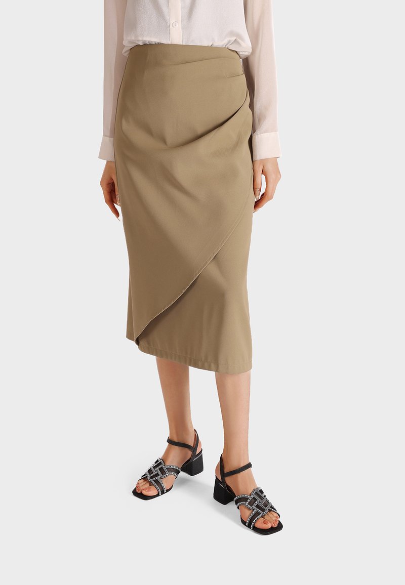 Gonna midi beige con un design drappeggiato, realizzata in tessuto morbido. Abbinata a sandali neri con tacco a blocco dotati di cinturini decorativi.