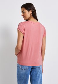 Top rosa de manga corta con cuello redondo y un corte holgado, combinado con jeans de mezclilla azul claro. Textura suave con un sutil brillo.