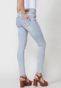 Jeans ajustados de color azul claro con cintura alta, bolsillos traseros y costuras en contraste; combinados con sandalias de plataforma marrones.
