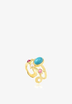 Bague en or avec une bande irrégulière présentant quatre pierres : un grand turquoise, un petit rouge, un rose et une perle blanche, sur fond blanc.
