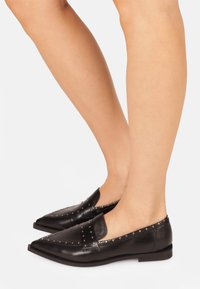 Black leather loafers with pointed toe, studded accents along the instep and heel, and a flat sole. Smooth texture and sleek design.
