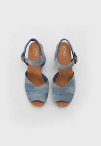 Blå denim kilehæle med åben tå og ankelrem. Har en brun tekstureret indersål og en spænde lukning for justerbarhed.