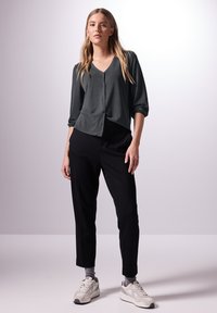 Graue V-Ausschnitt-Bluse mit Knopfleiste, Dreiviertelärmeln, kombiniert mit schwarzen, schmal geschnittenen Hosen und hellgrauen Sportschuhen.