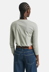 Langærmet, lysegrå skjorte med rund halsudskæring. Kombineret med mørkeblå denim jeans. Synlig brun læderbælte i midjen.