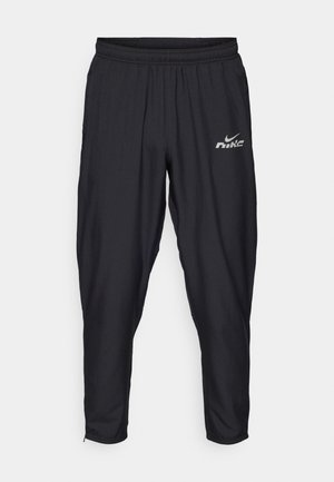 Pantalones deportivos negros con cintura elástica, diseño ajustado, bolsillos laterales y un logo reflectante de Nike en la parte delantera.