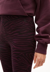 Paarse leggings met een zwart zebra streep patroon, gemaakt van rekbaar materiaal, gecombineerd met een bijpassende paarse oversized hoodie.