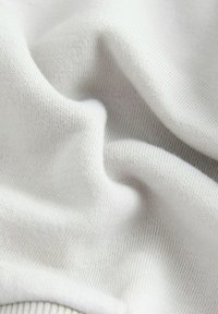 Hellgrauer Strickstoff mit einer glatten Oberfläche, der feine, gleichmäßige Rippen aufweist. Das Material wirkt weich und dehnbar.