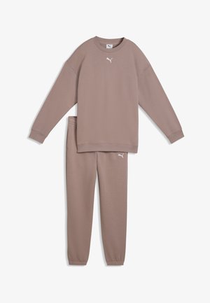 Długi rękaw bluzy w kolorze jasnopurpurowym oraz dopasowane spodnie dresowe z białymi logo Puma na piersi i lewym udzie.