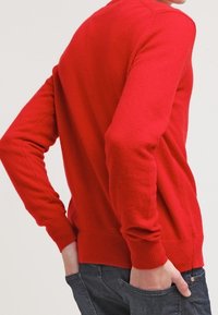 Czerwona sweter z dzianiny, z prążkowanymi mankietami i dołem. Dopasowany krój z długimi rękawami, widoczny z tyłu.