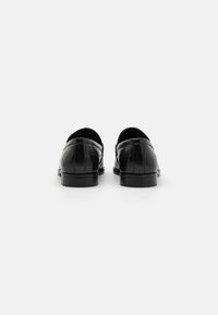 Zapatos de cuero negro con textura de cocodrilo, punta redondeada y un tacón bajo y suave. Diseño simple y clásico sin adornos.