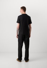 Svart t-skjorte med korte ermer og avslappet passform, kombinert med mørkegrå bukser. Myk tekstur, minimalistisk design og ingen synlige logoer eller mønstre.