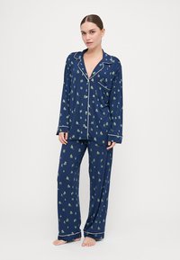 Navy blue pajama set in soft fabric with white piping, featuring a pattern of small green trees and red cabins on both top and pants.
