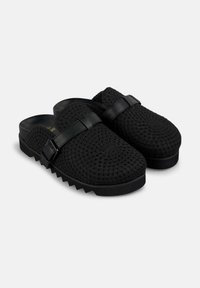 Scarpe slip-on nere con una trama intrecciata, dotate di una fascia in pelle nera liscia e di una suola testurizzata con un motivo a zigzag.