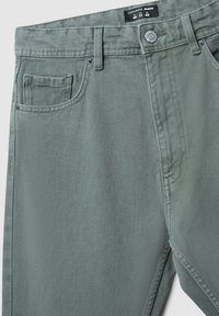 Jeans in denim verde con una finitura testurizzata, design a cinque tasche, chiusura con bottone metallico e dettagli cuciti. Etichetta della taglia visibile in vita.