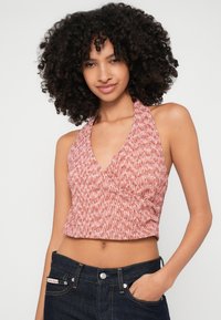 Virkat halter top i ett texturerat mönster av röd och vit. Har en djup V-ringning och en kort design, kombinerat med mörka jeans.