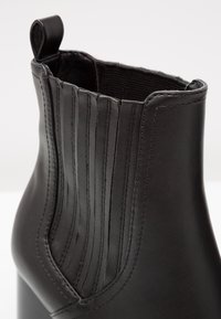 Czarne skórzane botki sięgające kostki z pionowym przeszyciem, gładką teksturą i pętelką u góry ułatwiającą zakładanie.