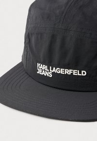 Fekete sapka könnyű anyagból, lapos karimával. A frontján hangsúlyos, fehér felirat található: "KARL LAGERFELD JEANS".