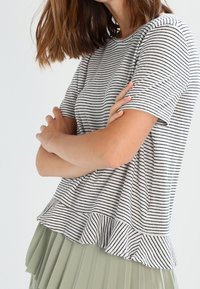 Top de manga corta a rayas en algodón gris y blanco, con un dobladillo con volantes. Combinado con una falda plisada de color verde claro.