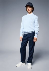 Lys blå kabelstrikket genser, marineblå bukser, hvite joggesko og svart caps med logo. Rent design, myk tekstur og avslappet passform.