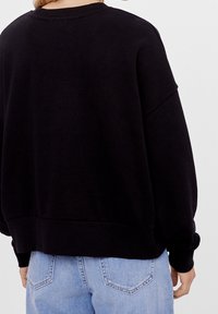 Svart oversize sweatshirt med rund halsringning, sänkt axel och ribbad mudd. Kombinerad med ljusblå denimjeans.