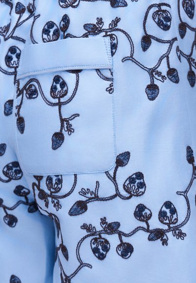 Ανοιχτό μπλε ύφασμα με σκούρο κεντητό βοτανικό μοτίβο και μια μικρή ορθογώνια τσέπη με καπάκι.